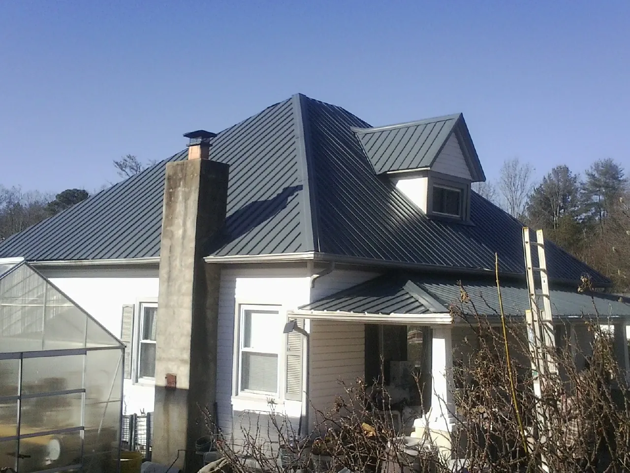 Dark blue standing seam metal roof on a white farmhouse with dormer — Slate & Tile Roof Repair by Roofing Brothers in Climax