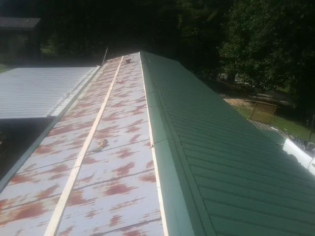Old rusted panels beside newly installed green metal roofing — Wind Damage Roof Repair by Roofing Brothers in Climax